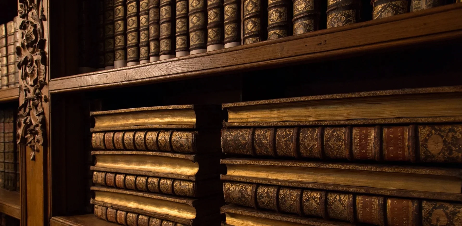 Reliures anciennes dorées alignées sur les rayonnages d’une bibliothèque en bois sculpté